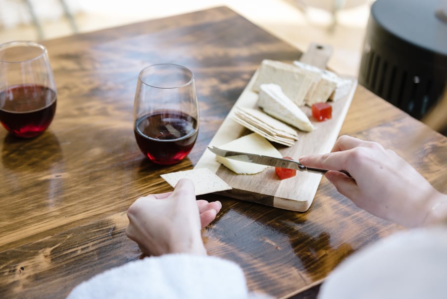 A person wearing a white robe enjoying a grazing board and a glass of red wine