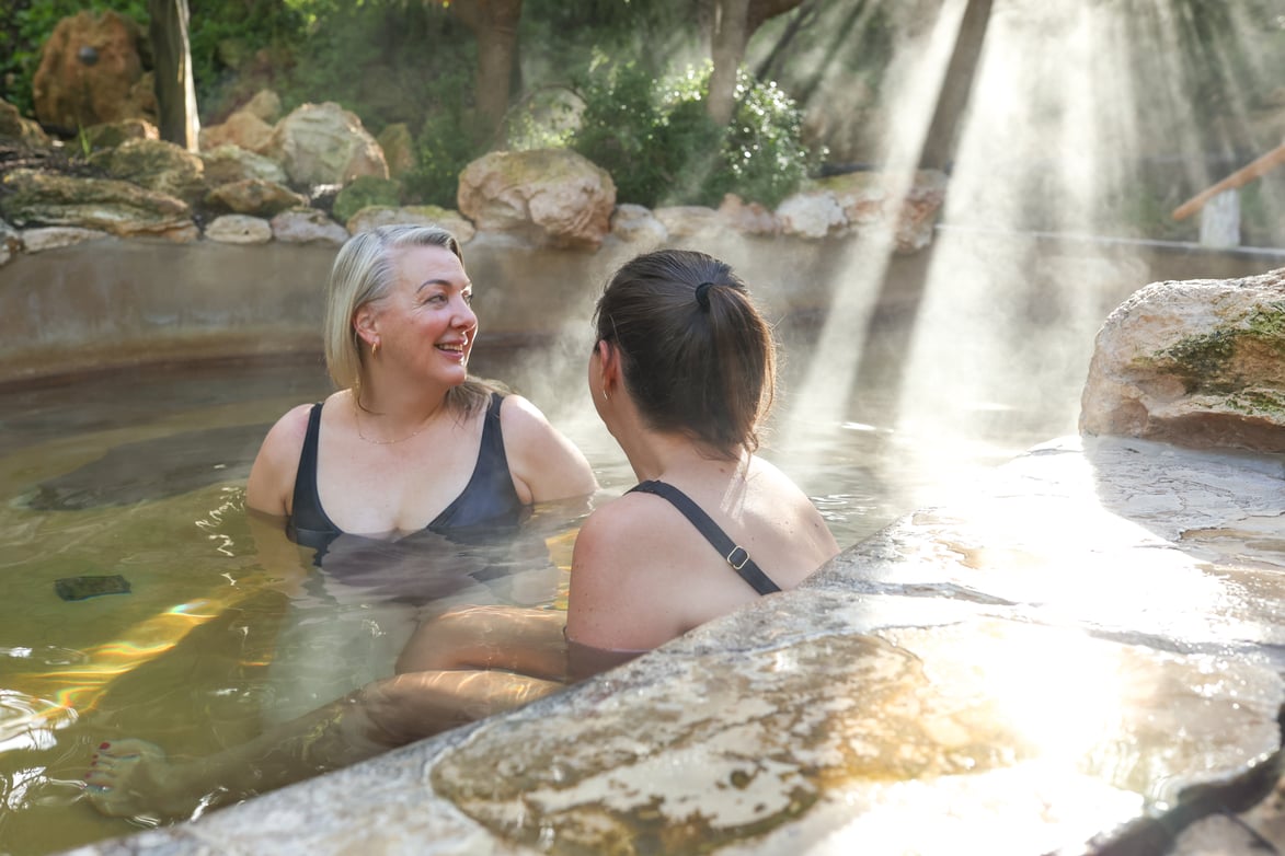 Two women bathing in hot springs while the sun shines down