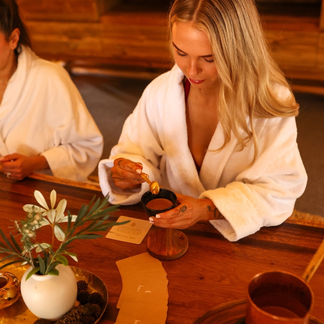 A woman in a white robe pouring cacao into a cup