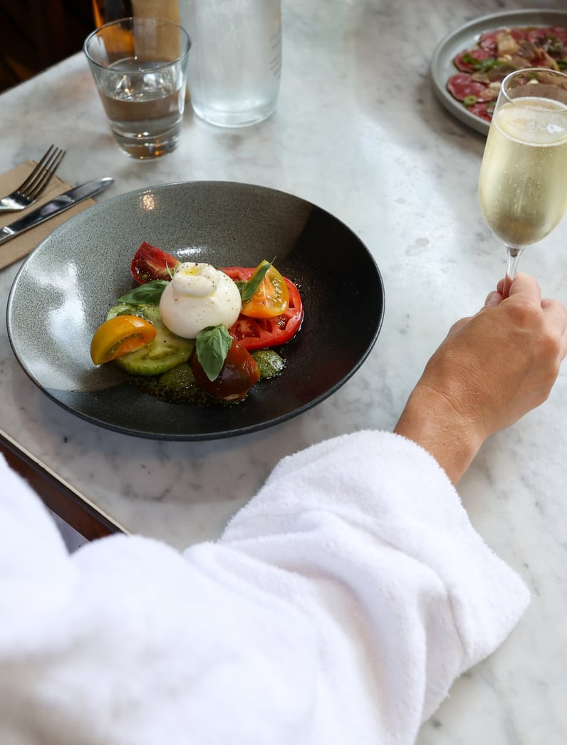 A person in a white robe eating a caprese salad