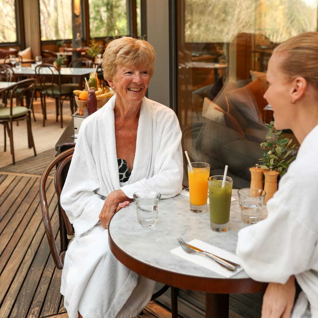 An older woman in a white robe enjoying a juice in the dining room