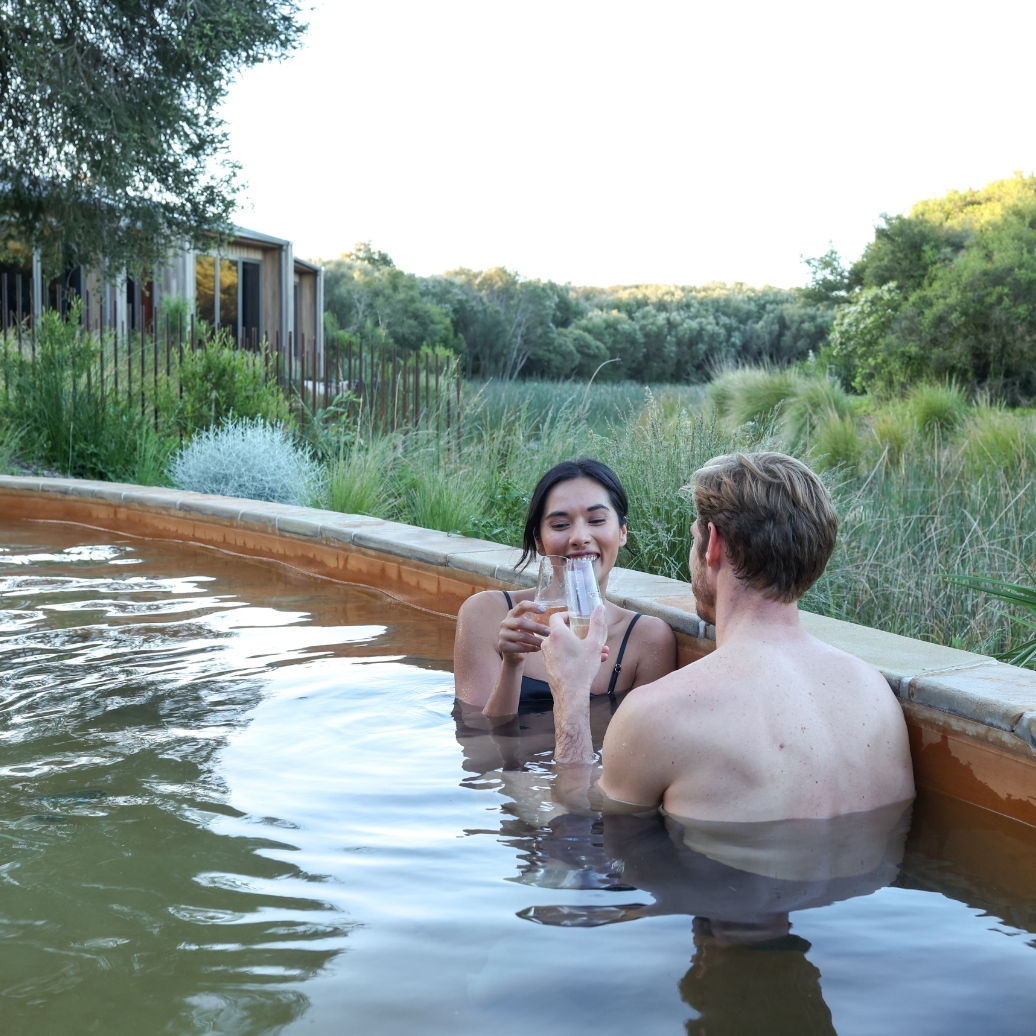 Two people drinking sparkling wine while in the hot spring pool in the Eco Lodges