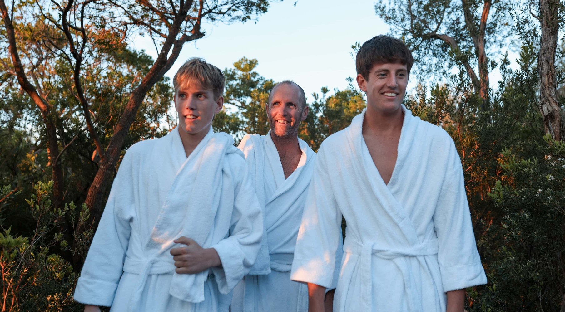 A father and two sons walking through nature in white robes