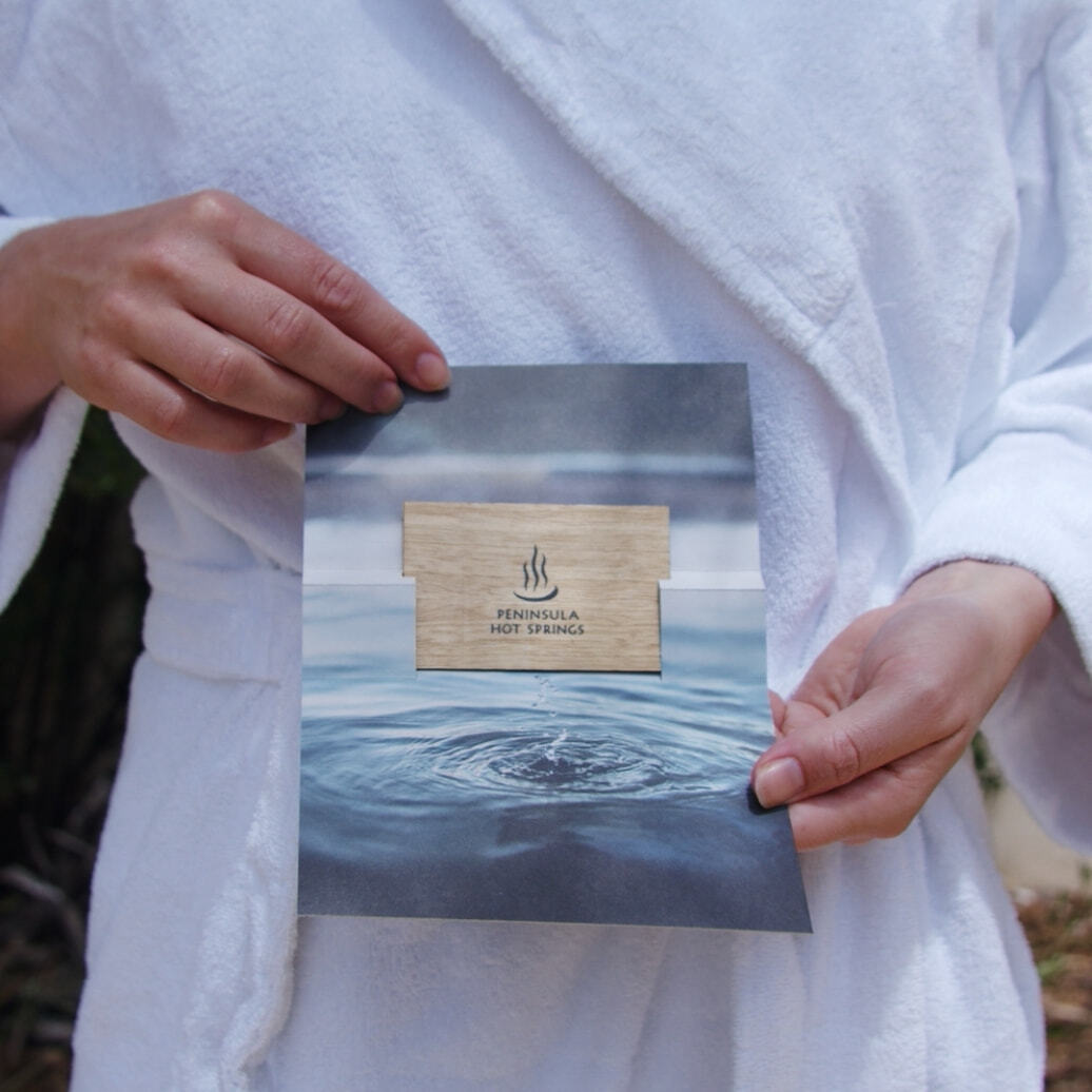 A person in a white robe holding open a Peninsula Hot Springs gift voucher
