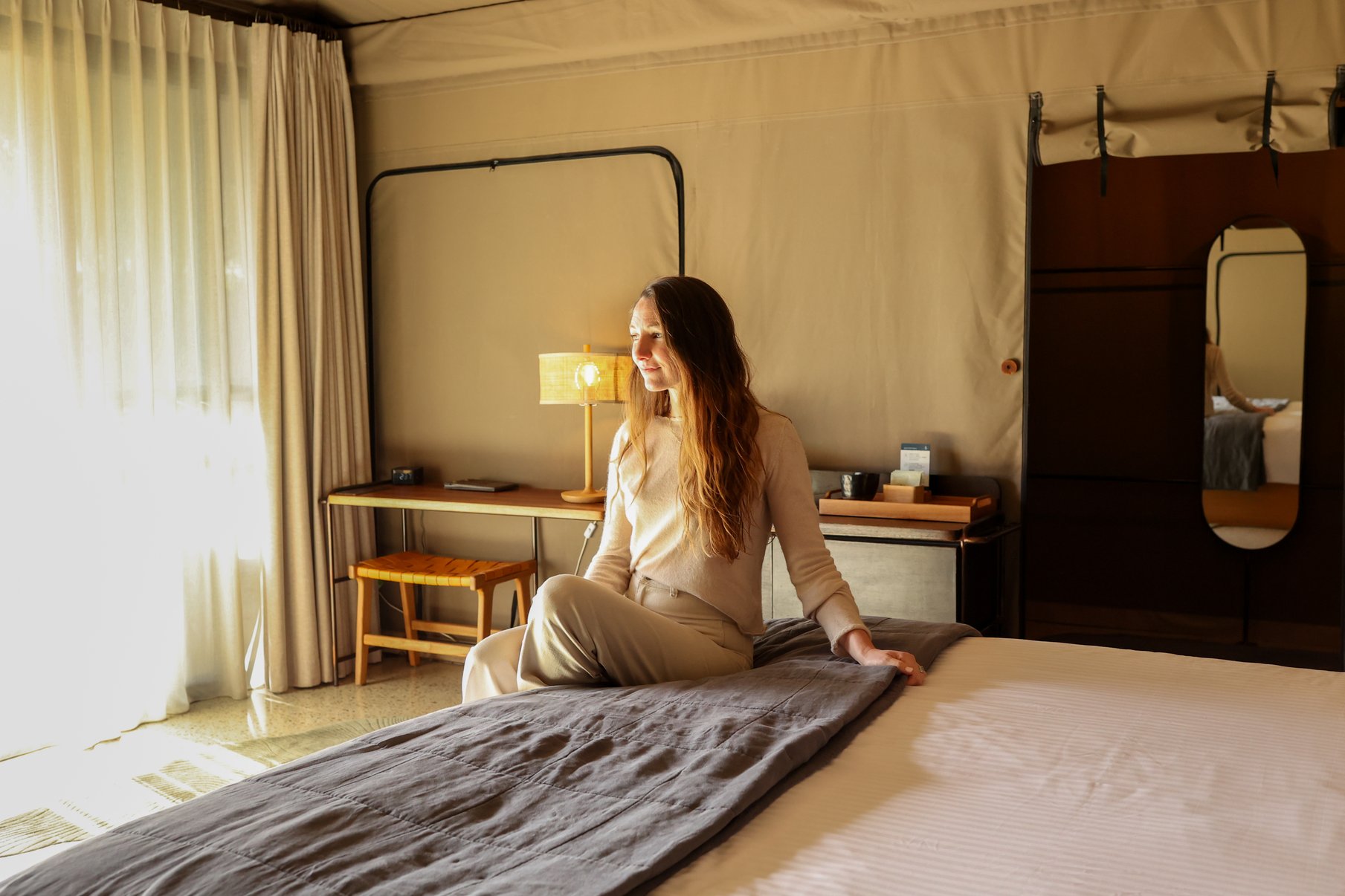 A woman sitting on a king sized bed in the Glamping tent