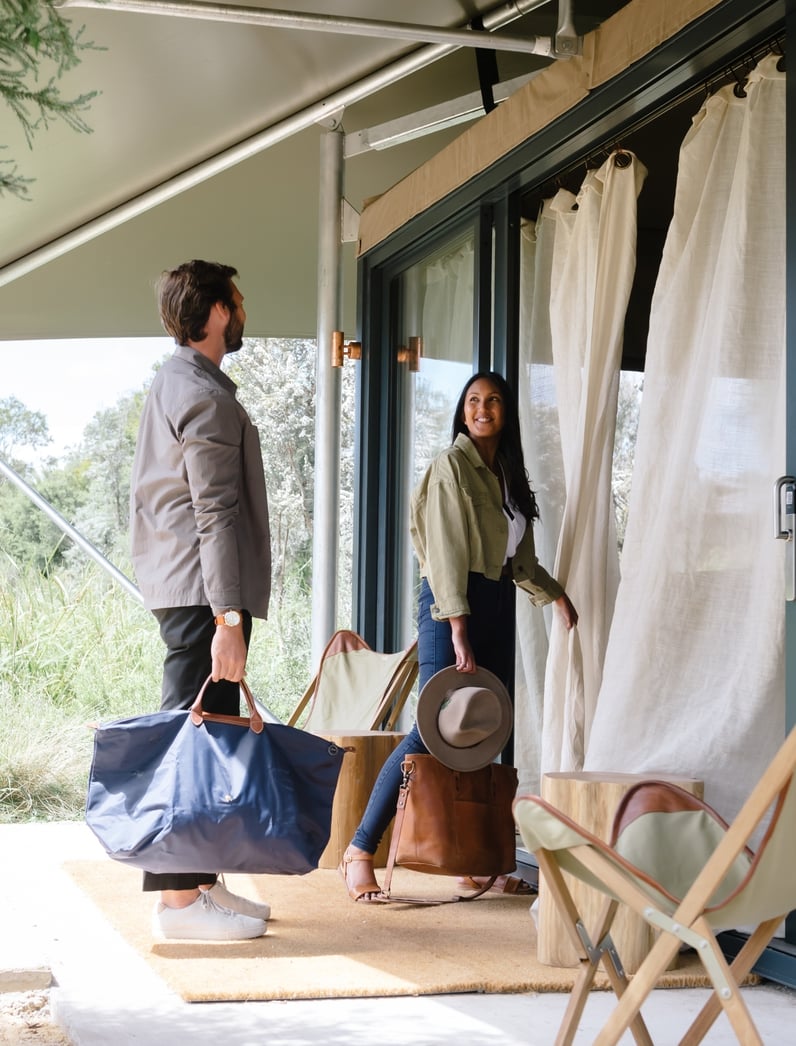 Two people with suitcases waling into a Glamping tent