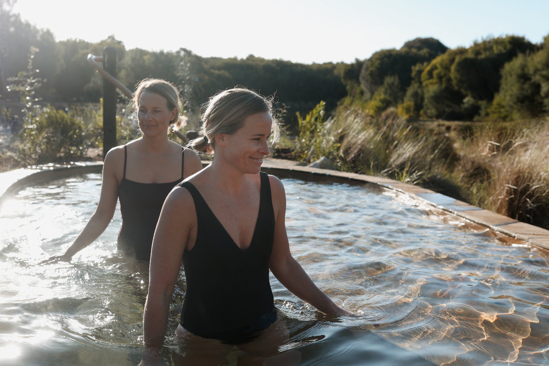 Two women in black bathers walking through a hot spring pool