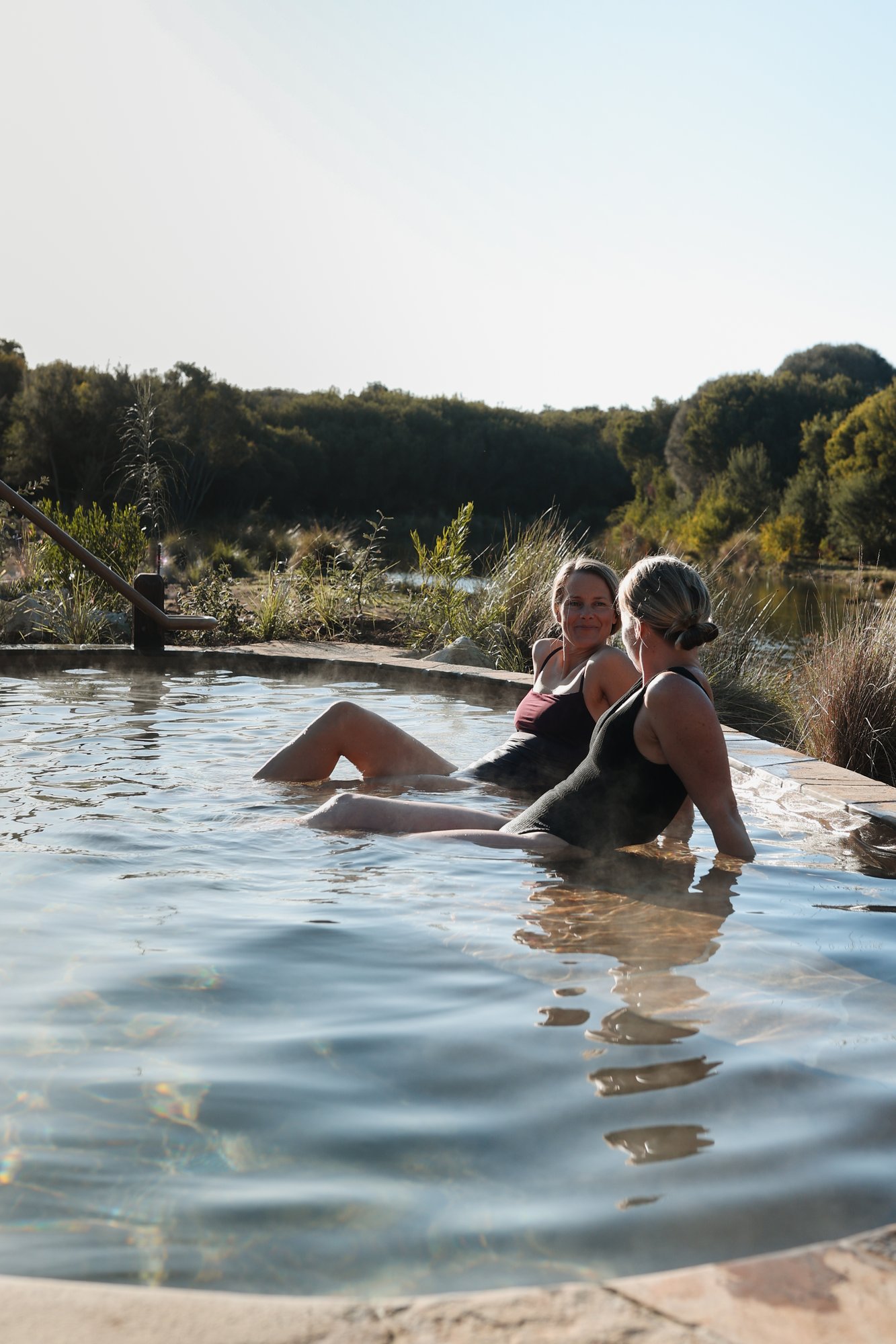 Two women lazing back in a shallow hot springs pool