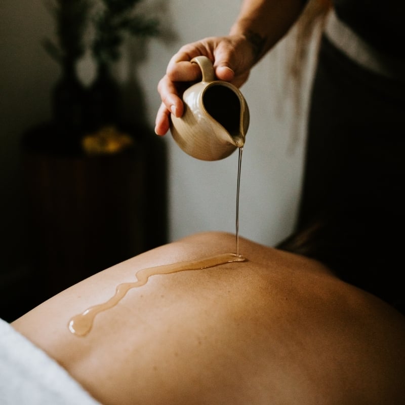 Oil dripping from a small jug onto a woman's back, preparing for massage