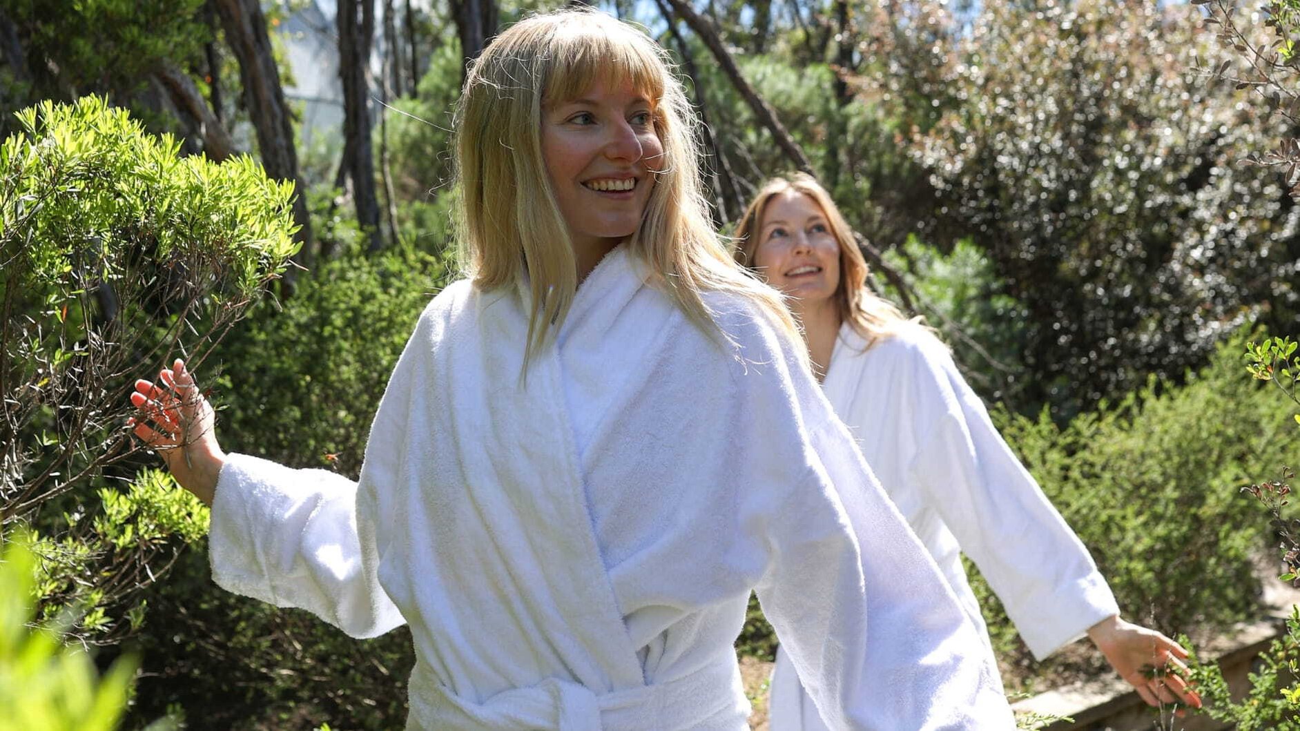 Two women in white robes walking through nature