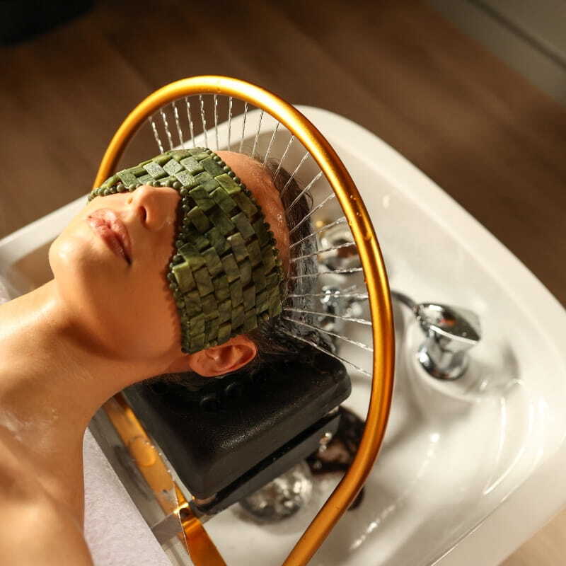 A woman having a Peninsula Head Spa treatment with a green eye mask covering her eyes
