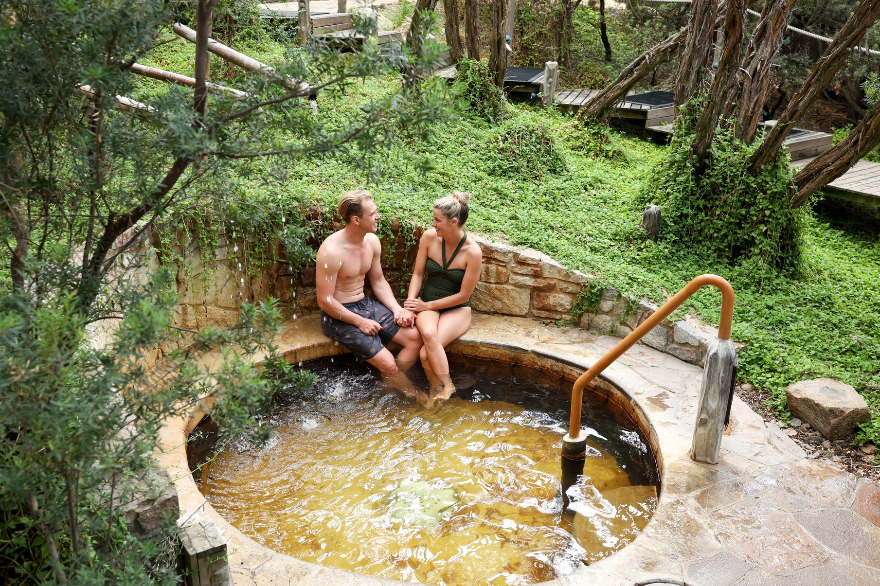 A man and woman sitting on the side of a hot springs pool