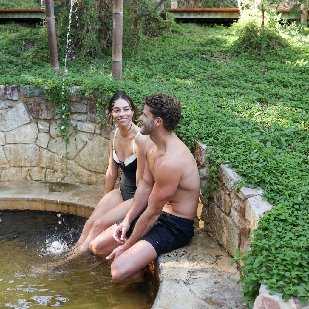 A man and a woman with their feet dangling in hot springs