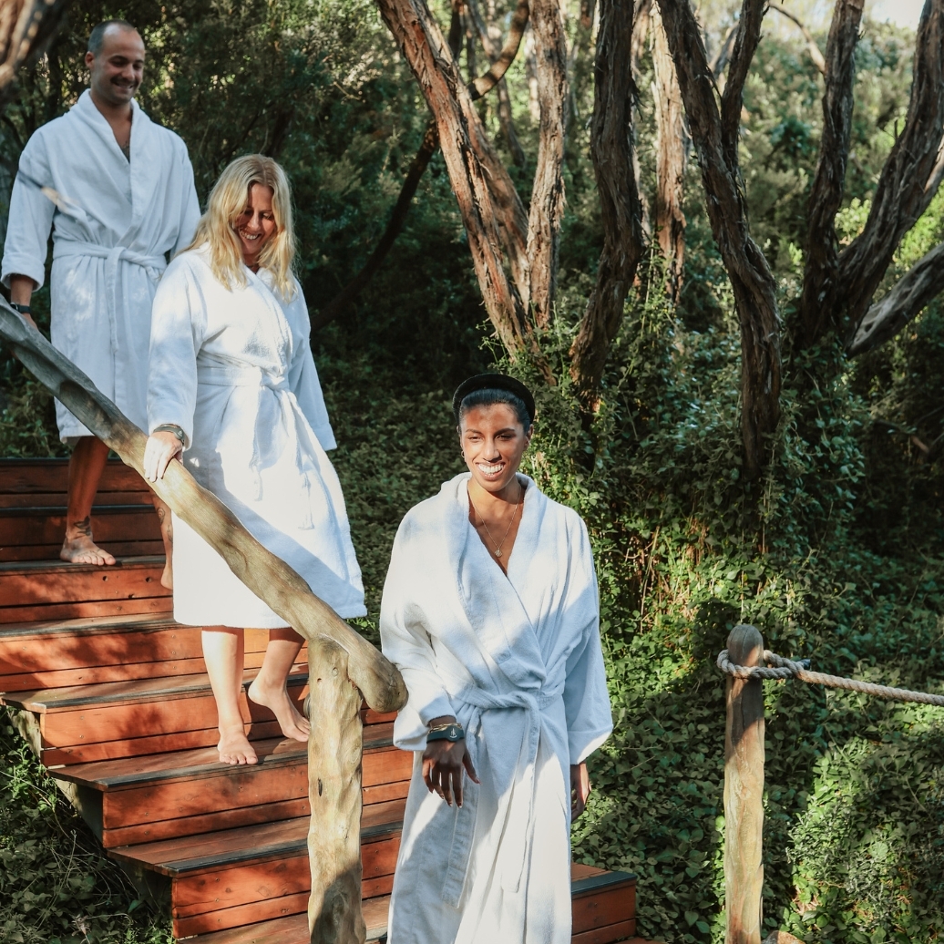 Three people in white robes walking down timber steps in nature