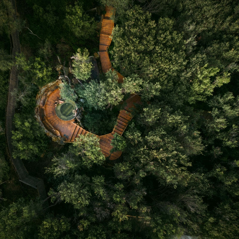 Aerial view of a circular geothermal pool nestled within dense native bushland at Peninsula Hot Springs, connected by timber boardwalks.