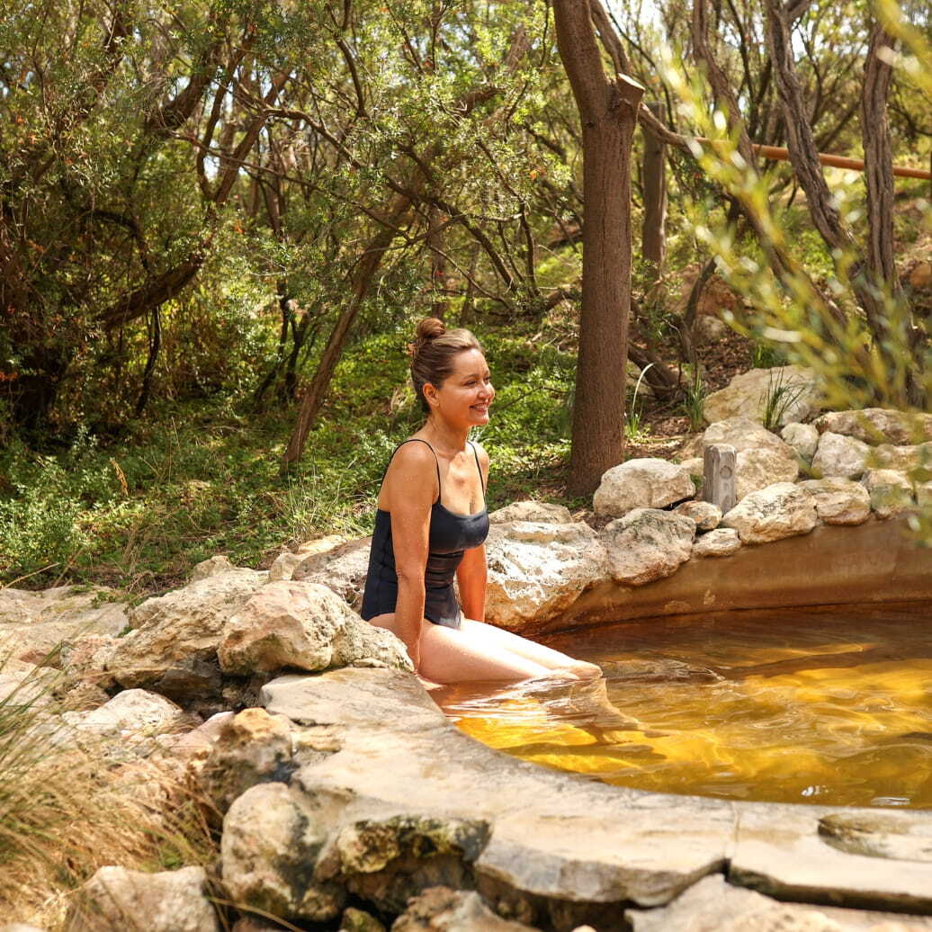 A woman sitting on the ledge with her legs dangling in hot springs