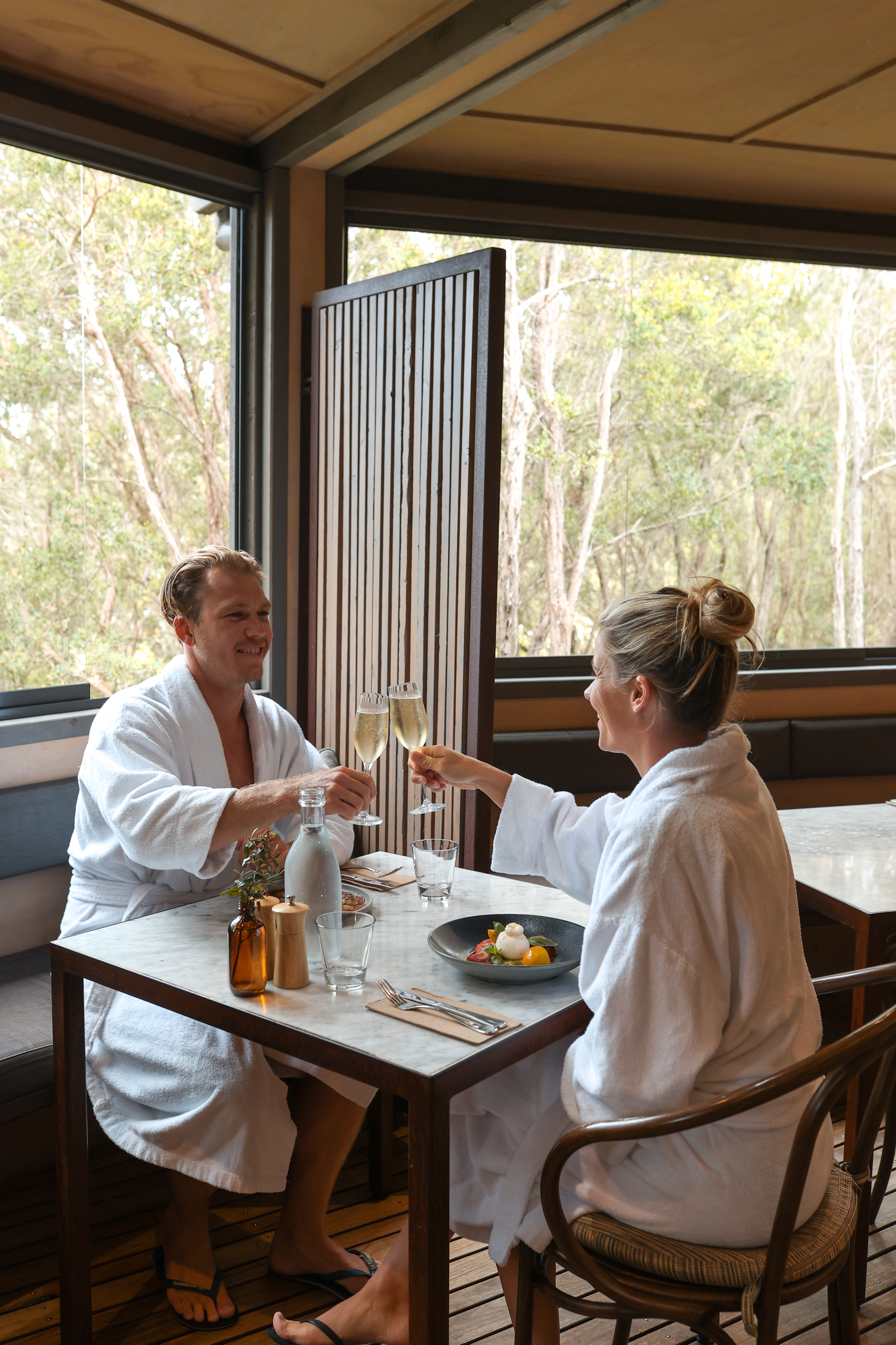 Two people sitting in white robes clinking sparkling wine glasses
