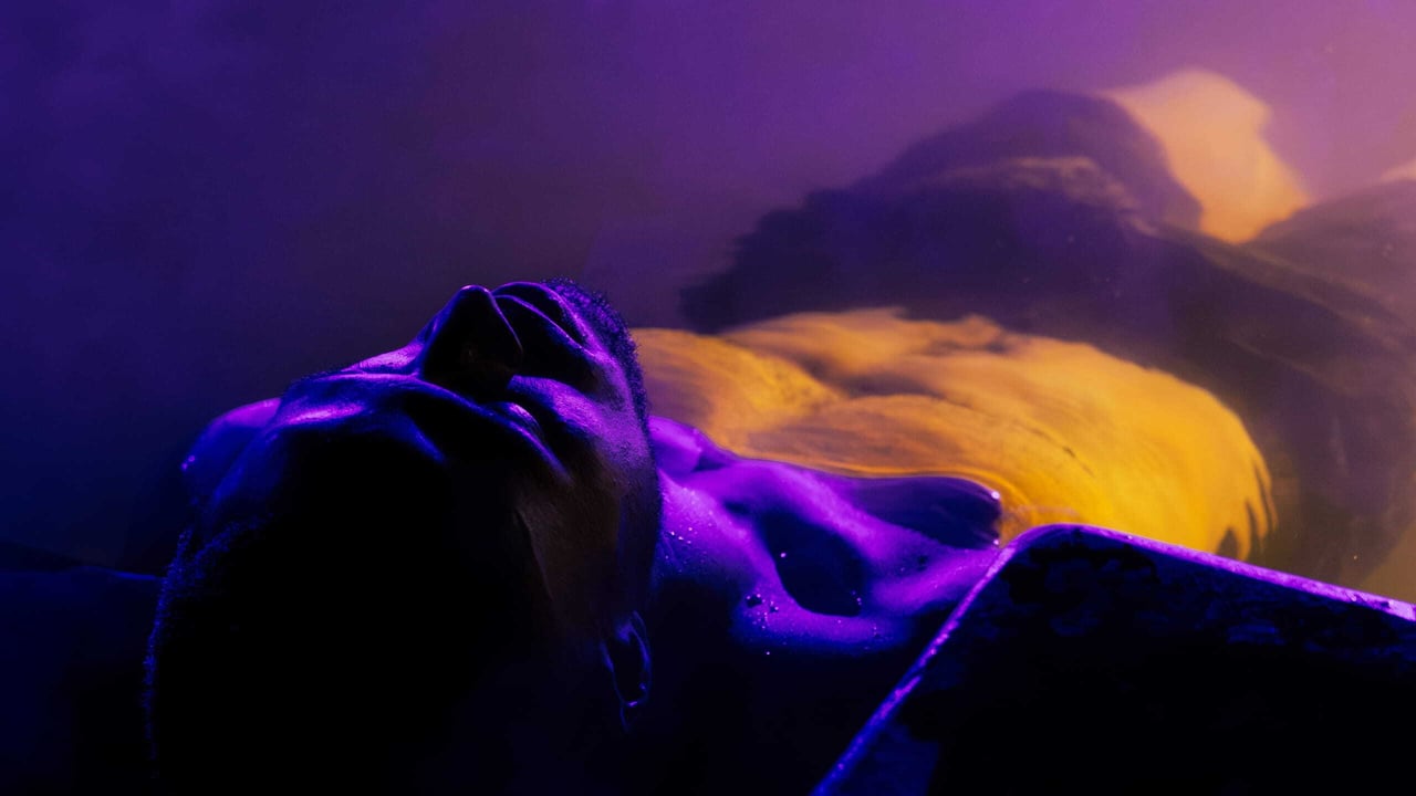 A man floating in a pool with indigo lighting reflecting from him