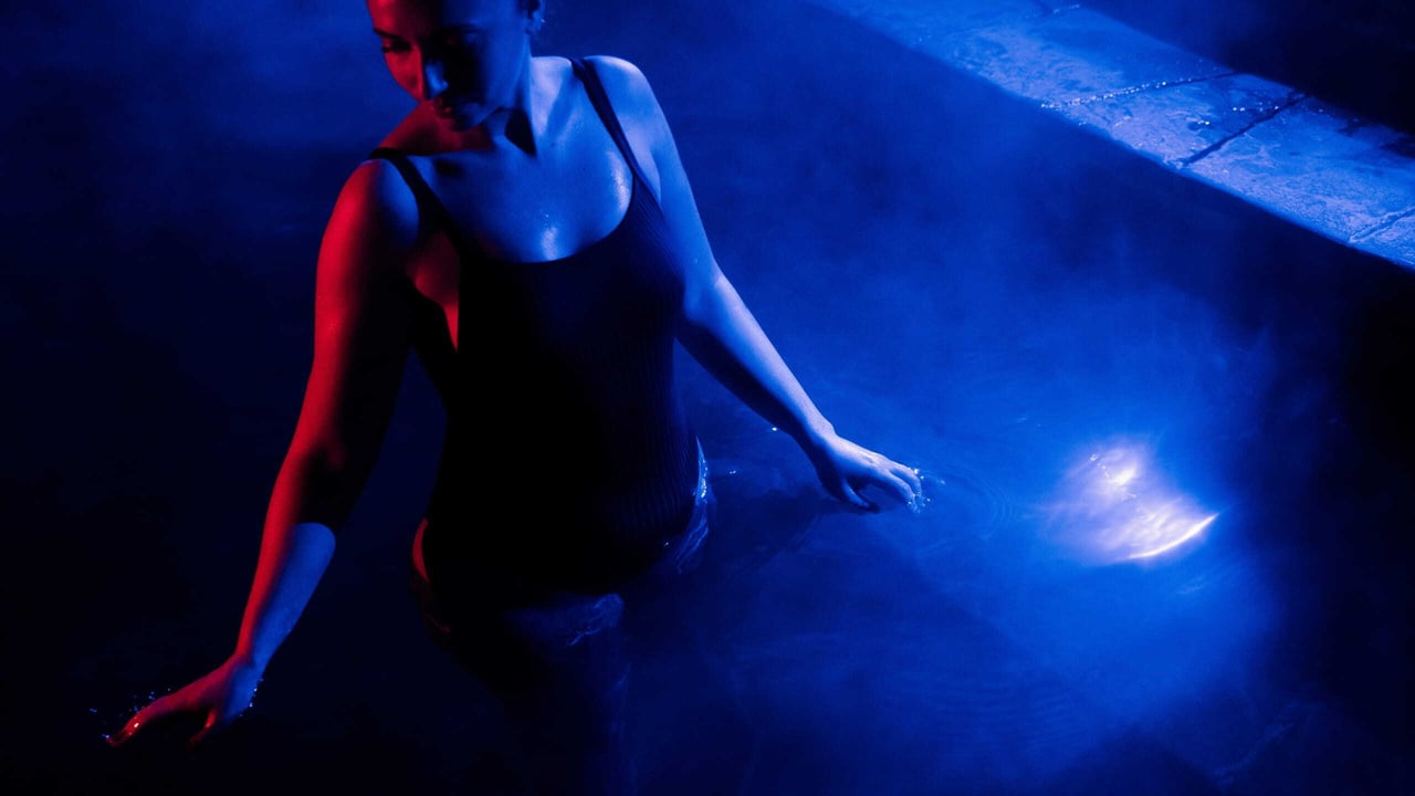 A woman walking through a hot spring with a blue light reflecting off the water