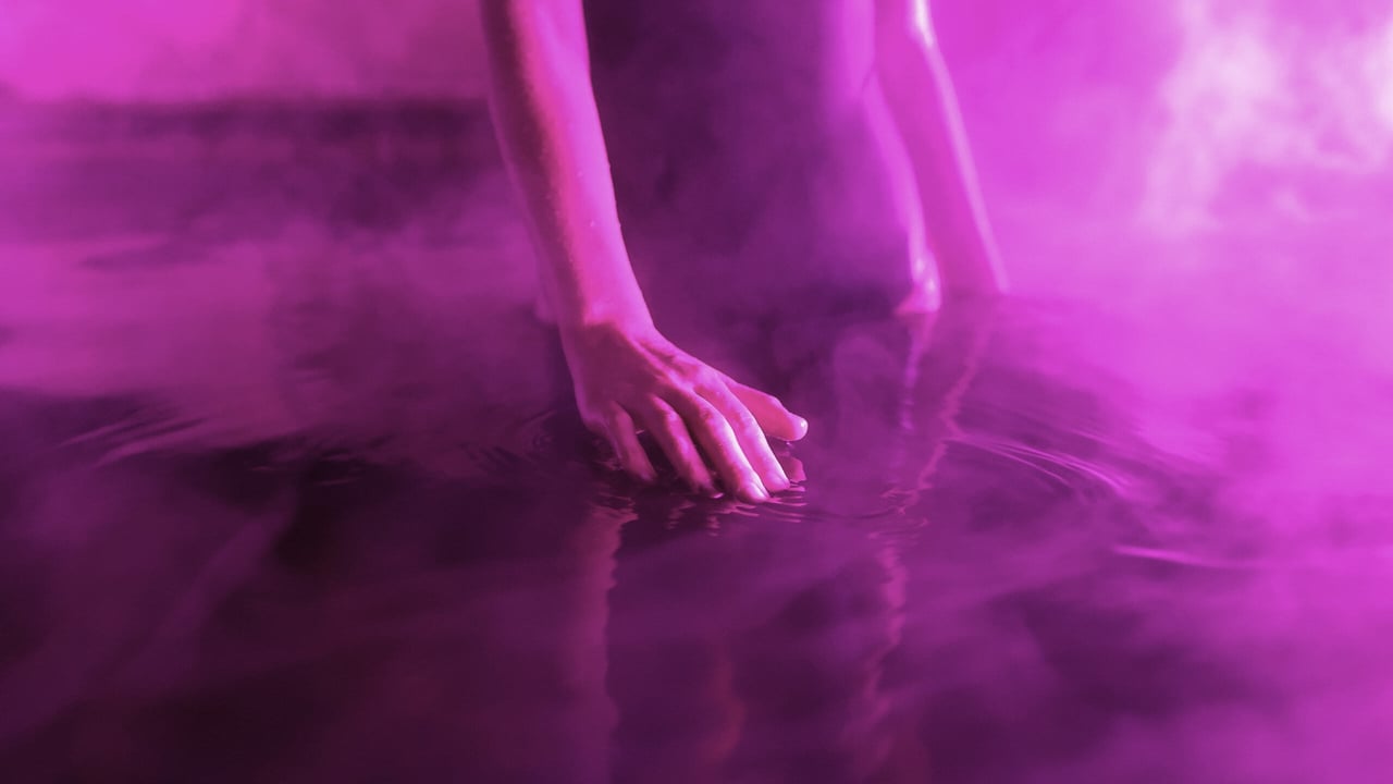A person placing their hand on the surface of a hot spring with a purple light surroudning them as part of the Seek the Heat winter campaign