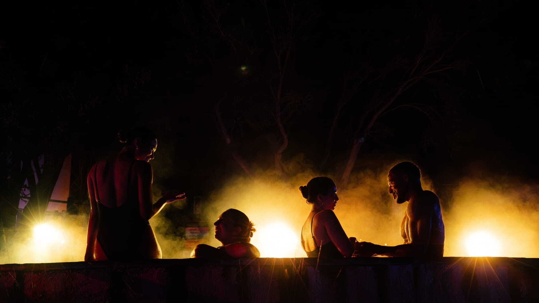 A group of friends in a yellow glowing hot springs pool as part of the Seek the Heat campaign