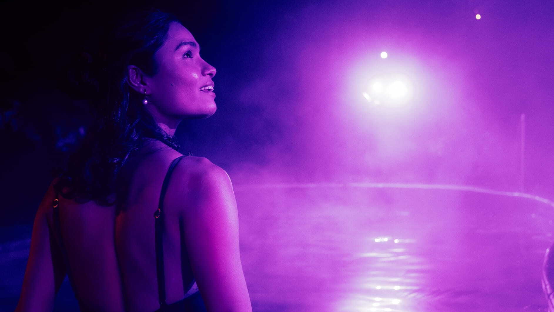 A woman bathing in a hot spring with a glowing purple light in front of her as part of the Seek the Heat campaign
