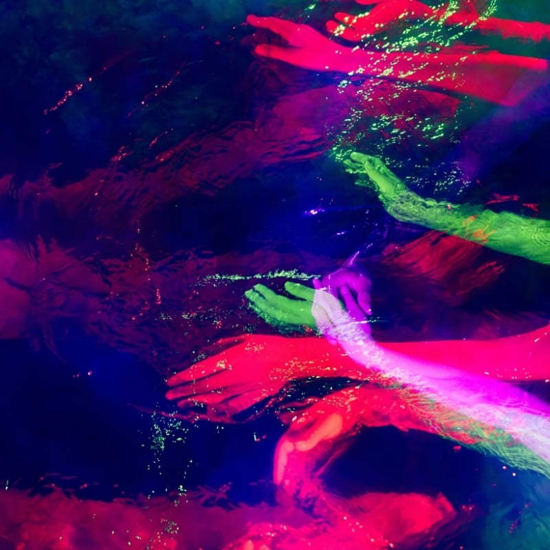 An edit of hands moving through water with various chakra-colours throughout