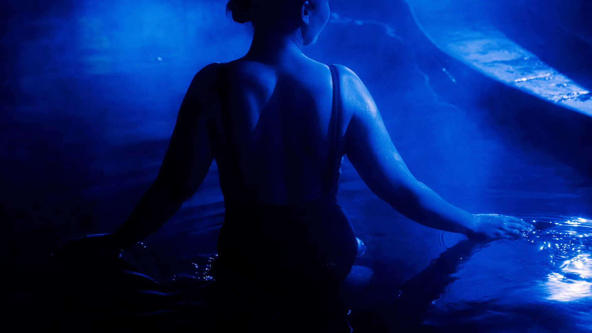 A woman in a hot spring pool with blue light reflecting as part of the Seek the Heat winter campaign