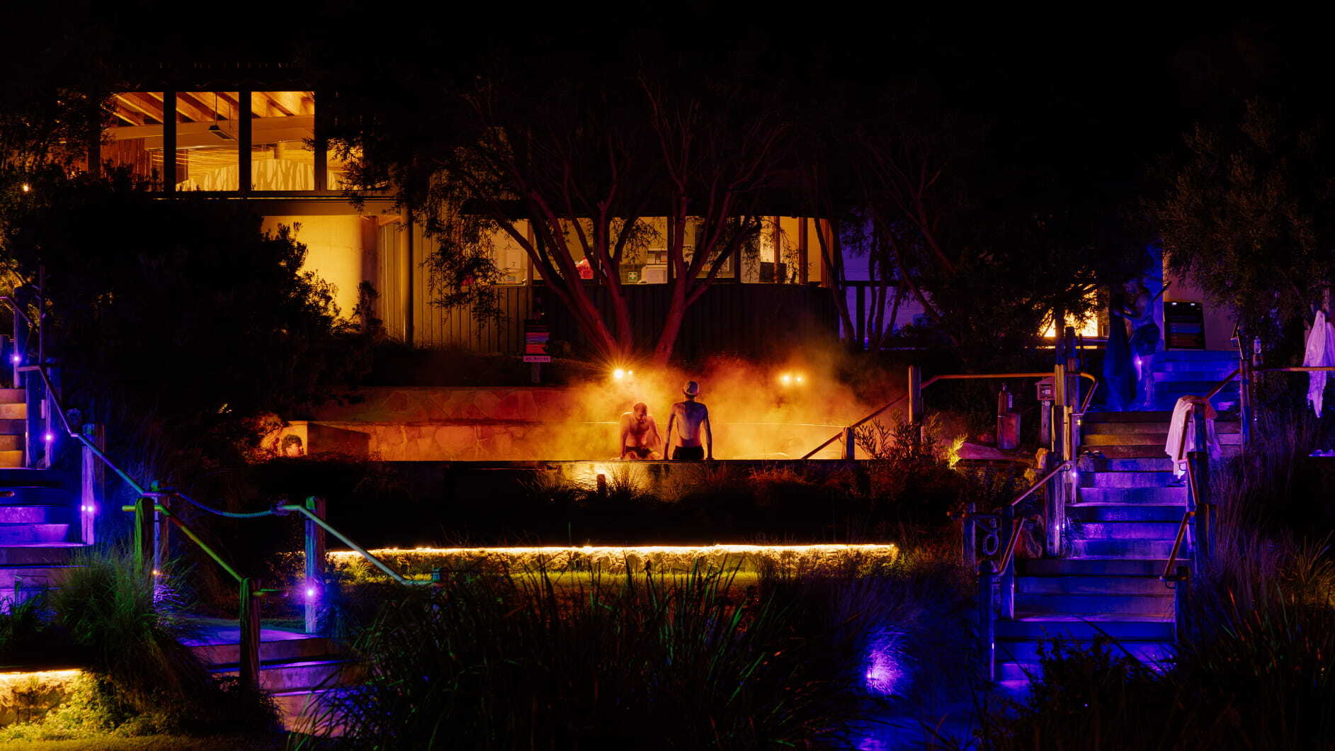 A wide shot of two people sitting in a golden lit pool as part of the Seek the Heat winter campaign
