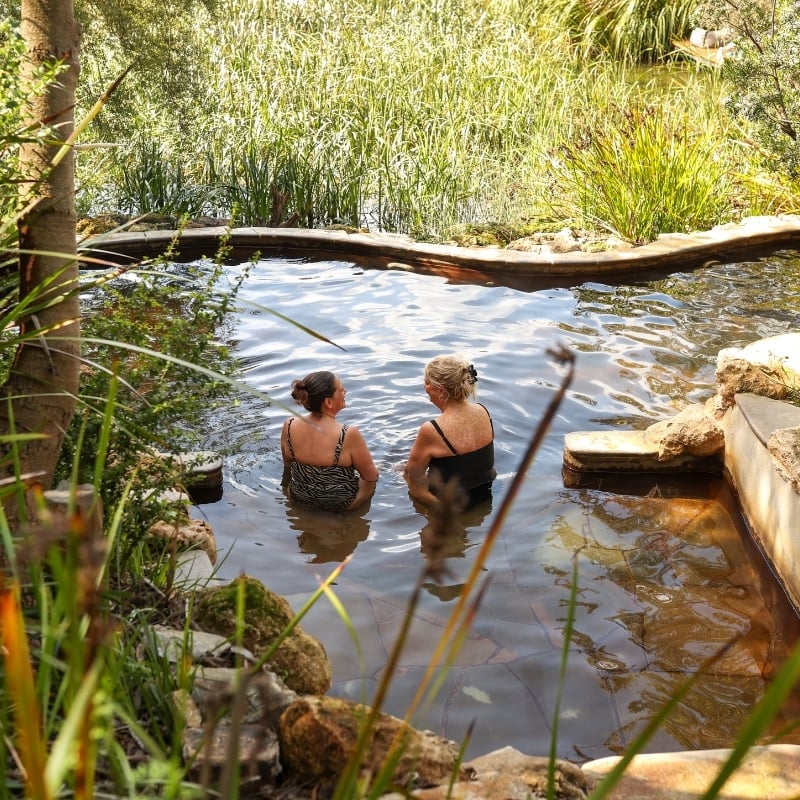 Two older women bathing in hot spring overlooking a lake