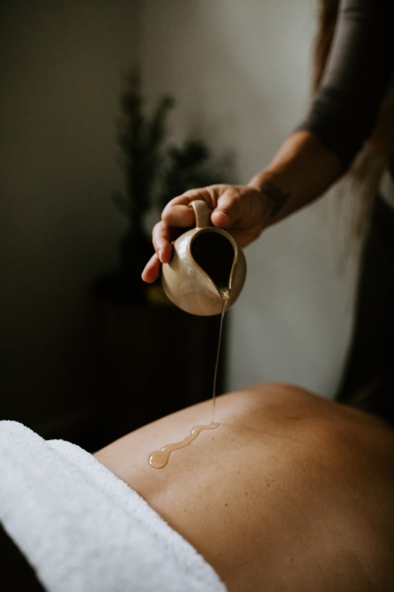 Oil dripping from a small jug onto a woman's back, preparing for massage