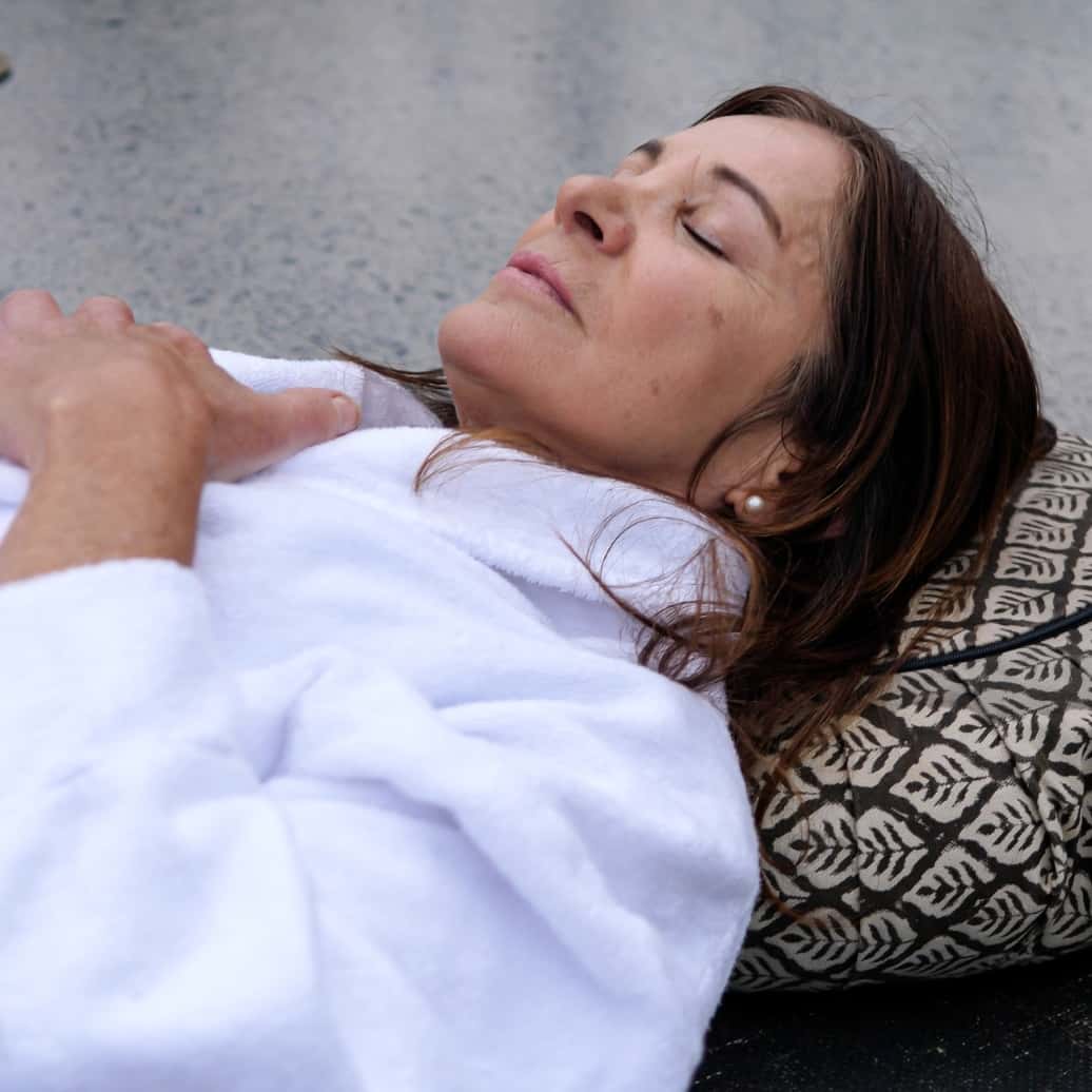 A woman lying down in a white robe with her eyes closed during a Stretch and Breathe class