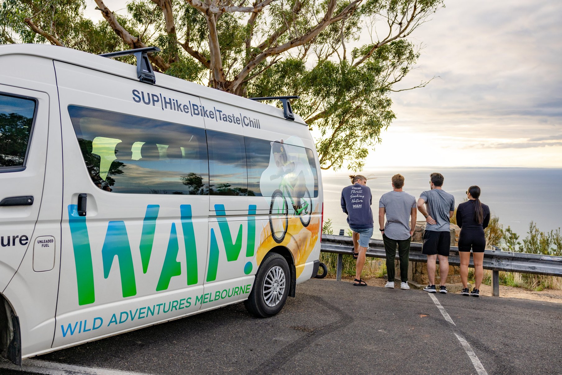 A bus with WAM branding and four travellers overlooking the view