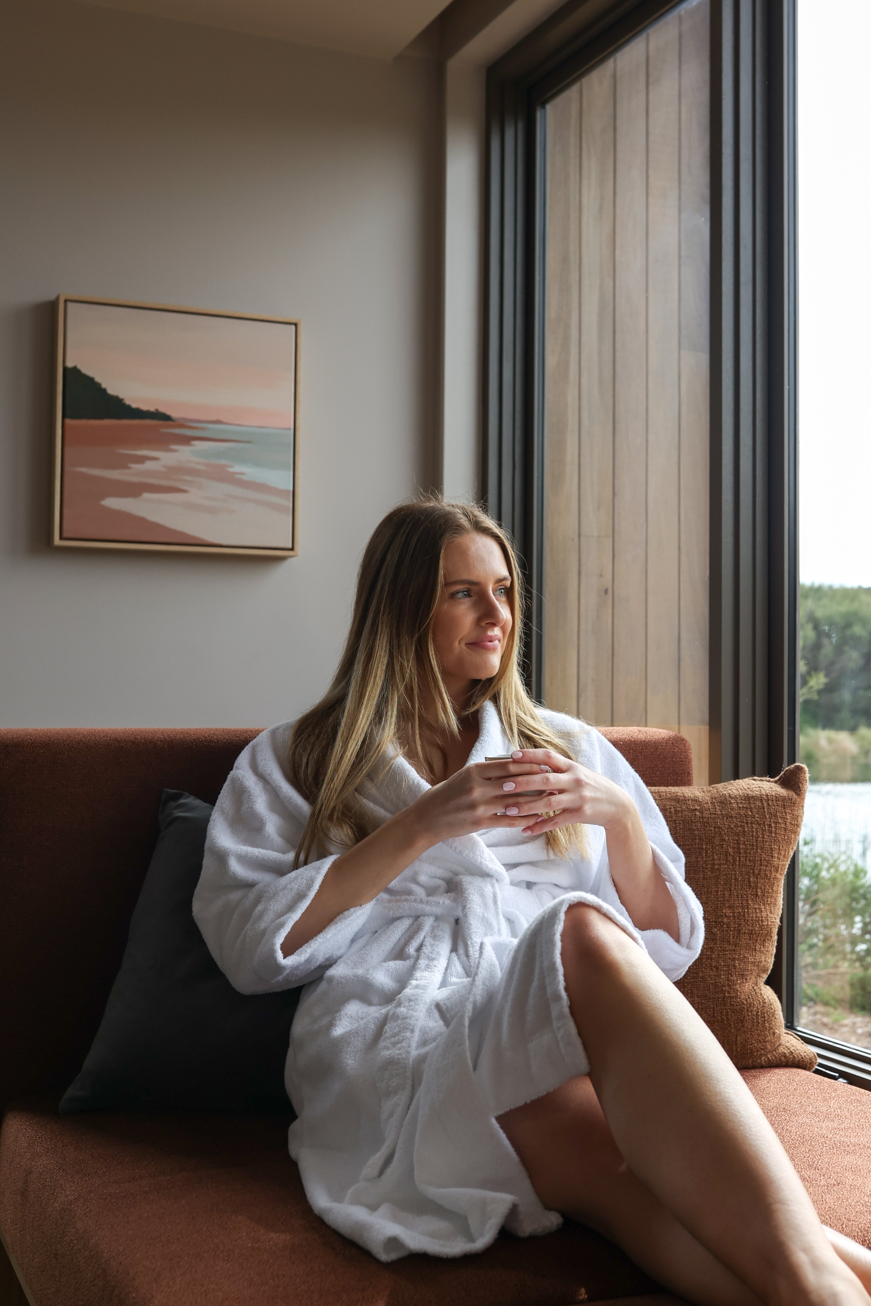 A woman holding a tea cup while lounging on a day bed in a white robe
